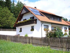 Une maison à deux étages avec un toit en pente, des panneaux solaires et des jardinières sur le balcon.