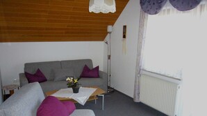 Een woonkamer met een grijze bank, paarse kussens, een salontafel met een plant, een vloerlamp en een radiator.