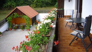Een terras met een houten constructie, zitplaatsen en potplanten.