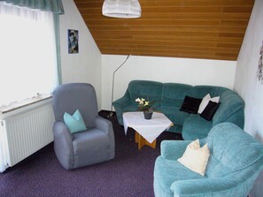 A living room with a grey armchair, teal sofa, and a small table with a plant.