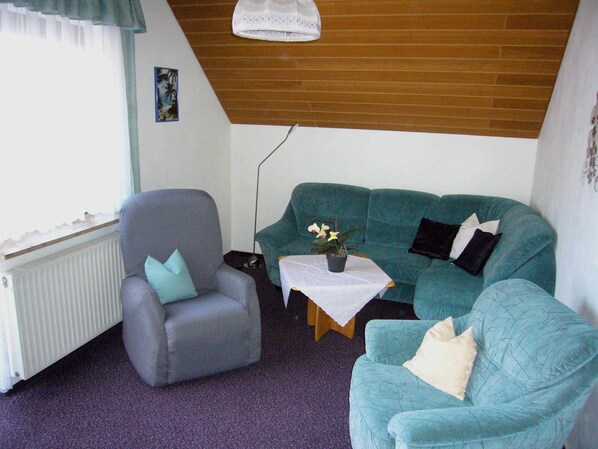 A living room with a grey armchair, teal sofa, and a small table with a plant.
