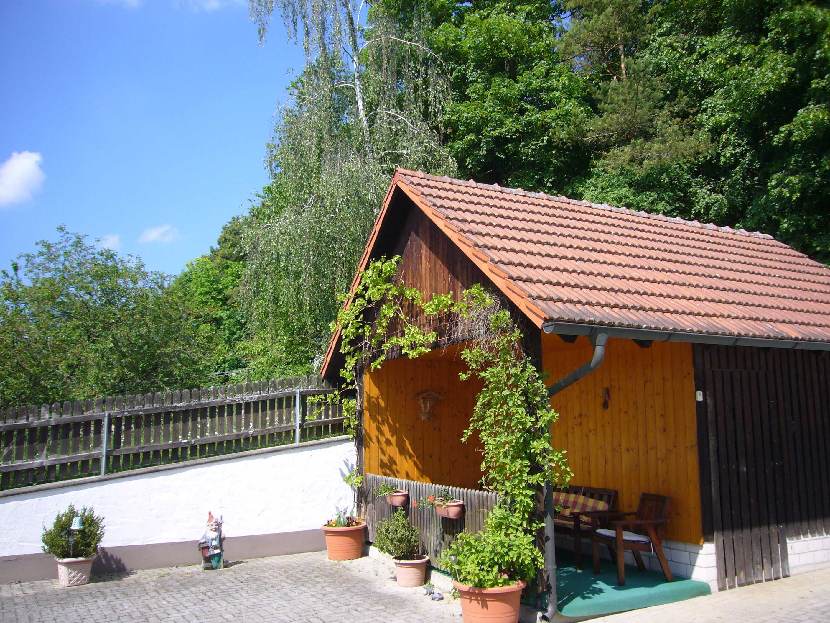 Eine kleine Holzhütte mit einem Ziegeldach, umgeben von Blumentöpfen und einer Bank.