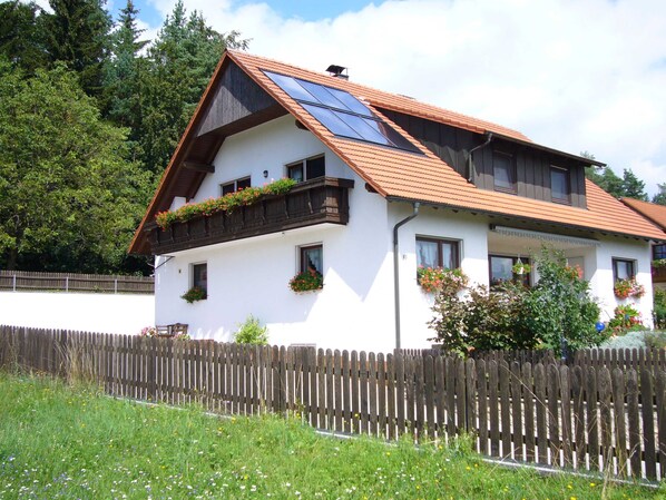 A two-story house with a sloped roof, solar panels, and flower boxes on the balcony.