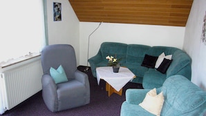 A living room with a grey armchair, teal sofa, and a small table with a plant.