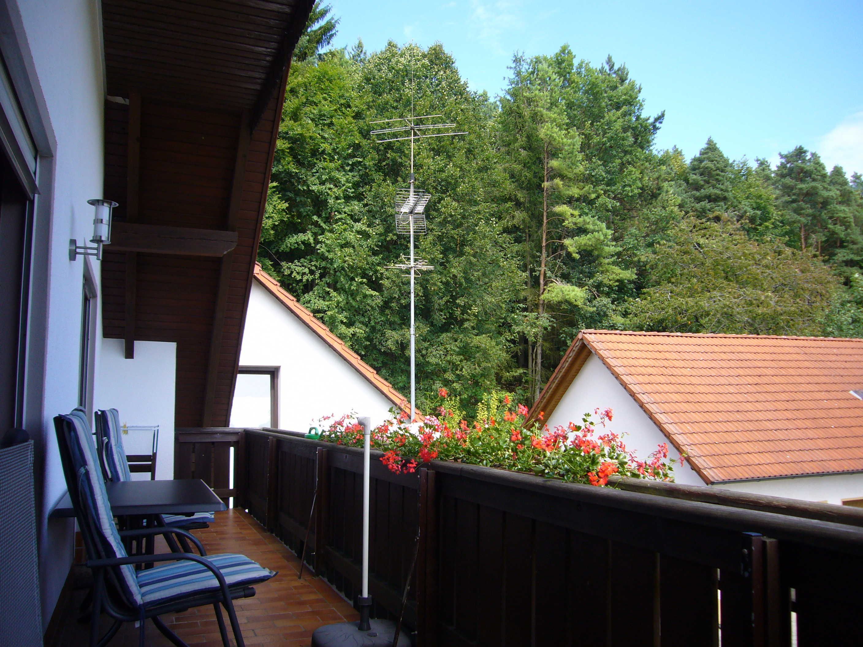 Un balcon aménagé avec du mobilier d’extérieur, une clôture en bois et une vue sur une colline boisée.