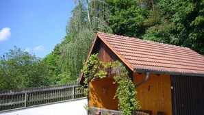 A small wooden cabin with a tiled roof, surrounded by potted plants and a bench.