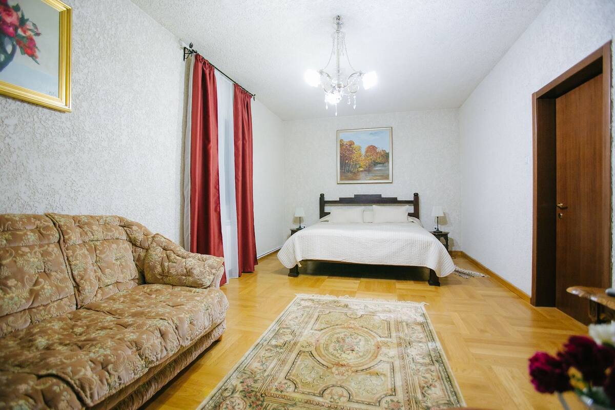Ein Schlafzimmer mit Bett, Sofa, einer Chandelieber, einem Gemälde und einer Tür.