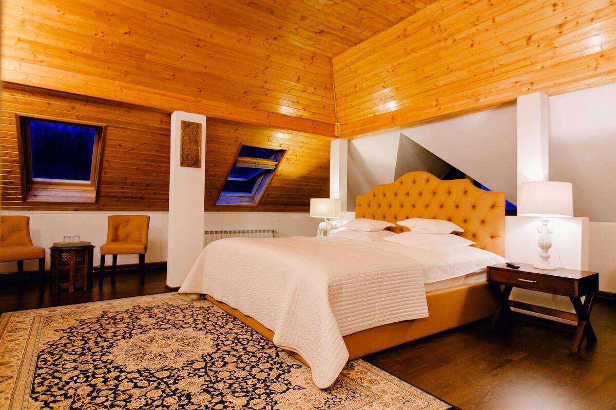Ein Schlafzimmer mit Holzboden, einem Bett mit gelbem Kopfteil, einem Nachttisch, einer Lampe und einem gemusterten Teppich.