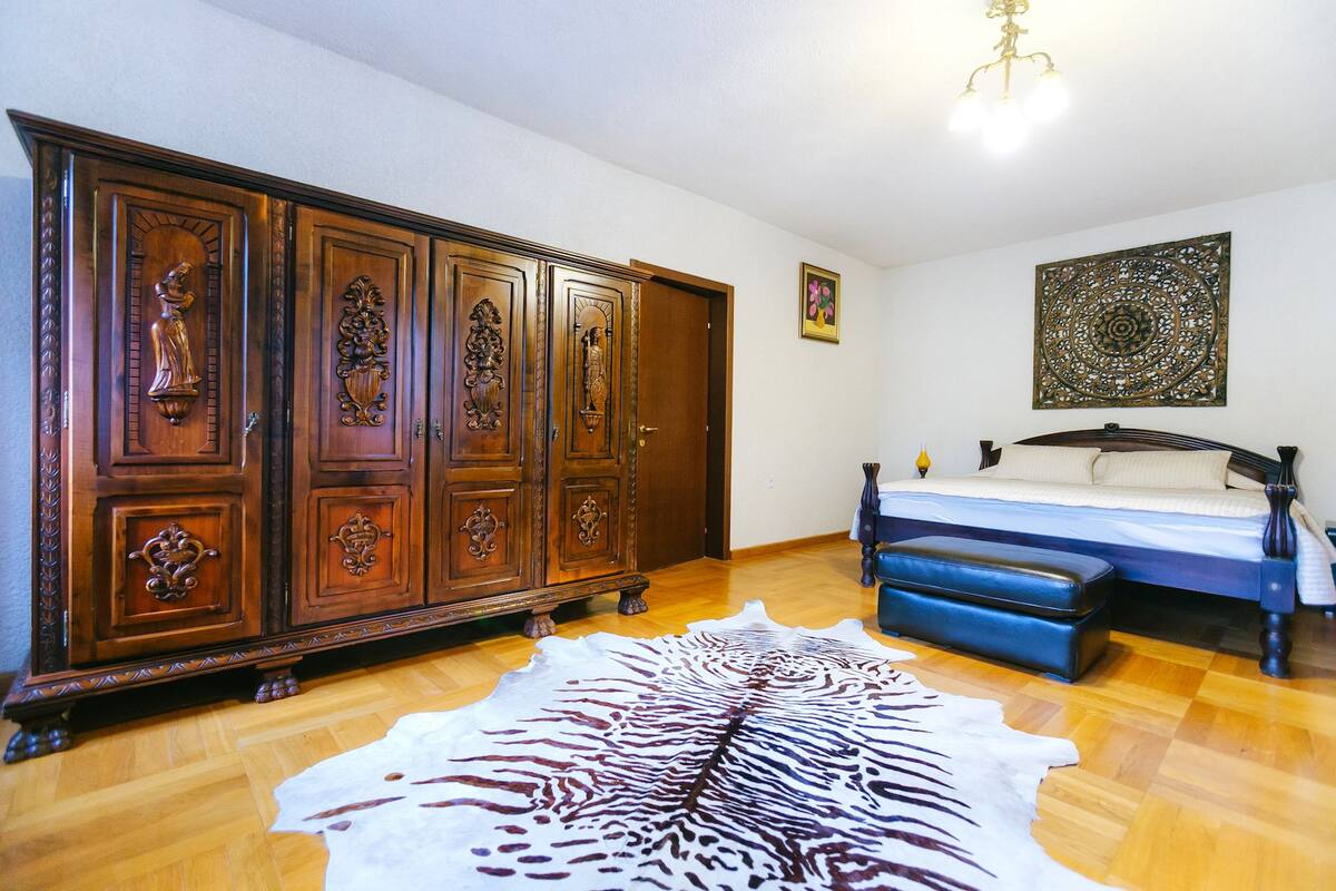 Ein Schlafzimmer mit einem großen, hölzernen Kleiderschrank, einem Bett mit blauer Bettwäsche, einem Zebra-Teppich und einem Wandbild.