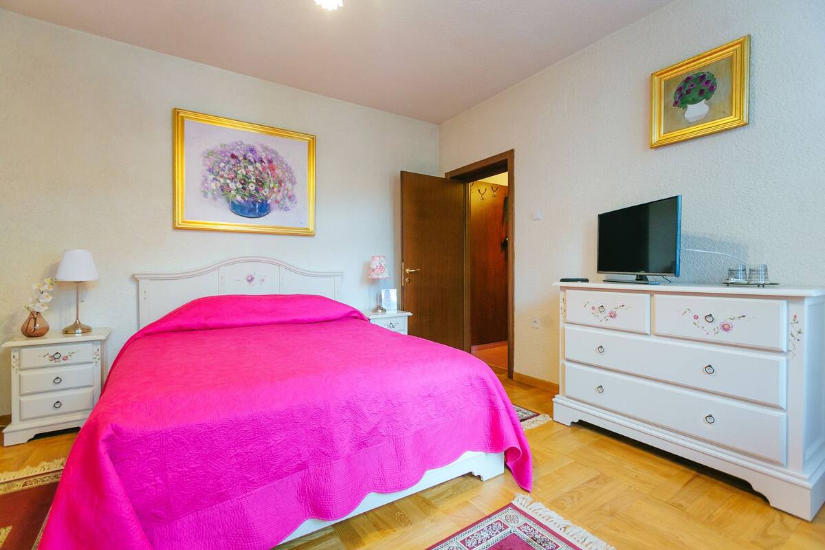 Ein Schlafzimmer mit einem Bett, einer Kommode, einem Fernseher und zwei gerahmten Bildern an der Wand.