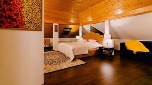 A bedroom with a wooden ceiling, a bed with a headboard, a nightstand, a lamp, a chair, and a sofa. - Casa Natalia (Sinaia)