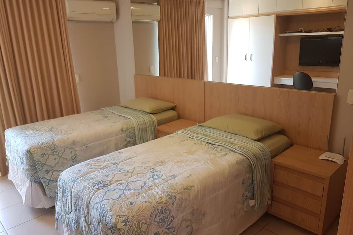 A hotel room with two beds, a wooden headboard, a TV, and a wardrobe.