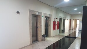 A hallway with tiled floors, elevators, and emergency exit signs. - Charming Furnished Studio Flat (Goiania)