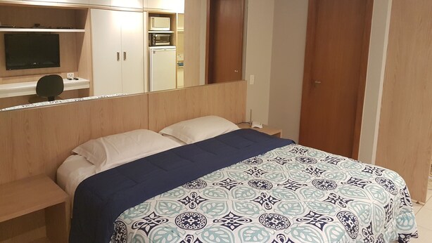 A bedroom with a bed, a desk, a television, and a wardrobe. - Charming Furnished Studio Flat (Goiania)
