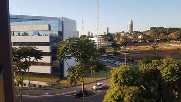 Um edifício moderno com fachada de vidro, um estacionamento com vários carros e uma vista clara da paisagem urbana ao redor.