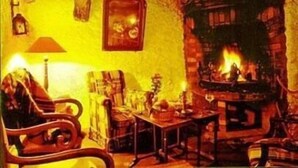 Una stanza accogliente con un camino, una sedia di legno, un tavolo e una libreria.