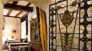 Un interno rustico caratterizzato da pareti in pietra a vista, soffitto in legno e zona pranzo con tavoli e sedie.