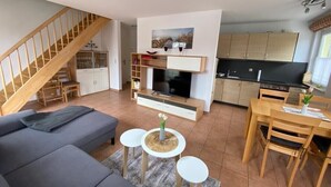 A modern living room with a sofa, TV, and dining area. - Bright, cozy apartment, centrally located in a quiet area of Zingst with WLAN (Mecklenburg-Vorpommern)