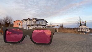 A pair of sunglasses with a dark frame and pink lenses, placed on a paved surface with a row of houses and a water tower in the background. - Bright, cozy apartment, centrally located in a quiet area of Zingst with WLAN (Mecklenburg-Vorpommern)