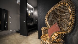 Un baño moderno con un espejo grande, un tocador negro y una silla de mimbre con cojín rojo.