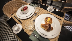 Una mesa de comedor con un croissant, un tazón de fresas, un vaso de agua y una taza.