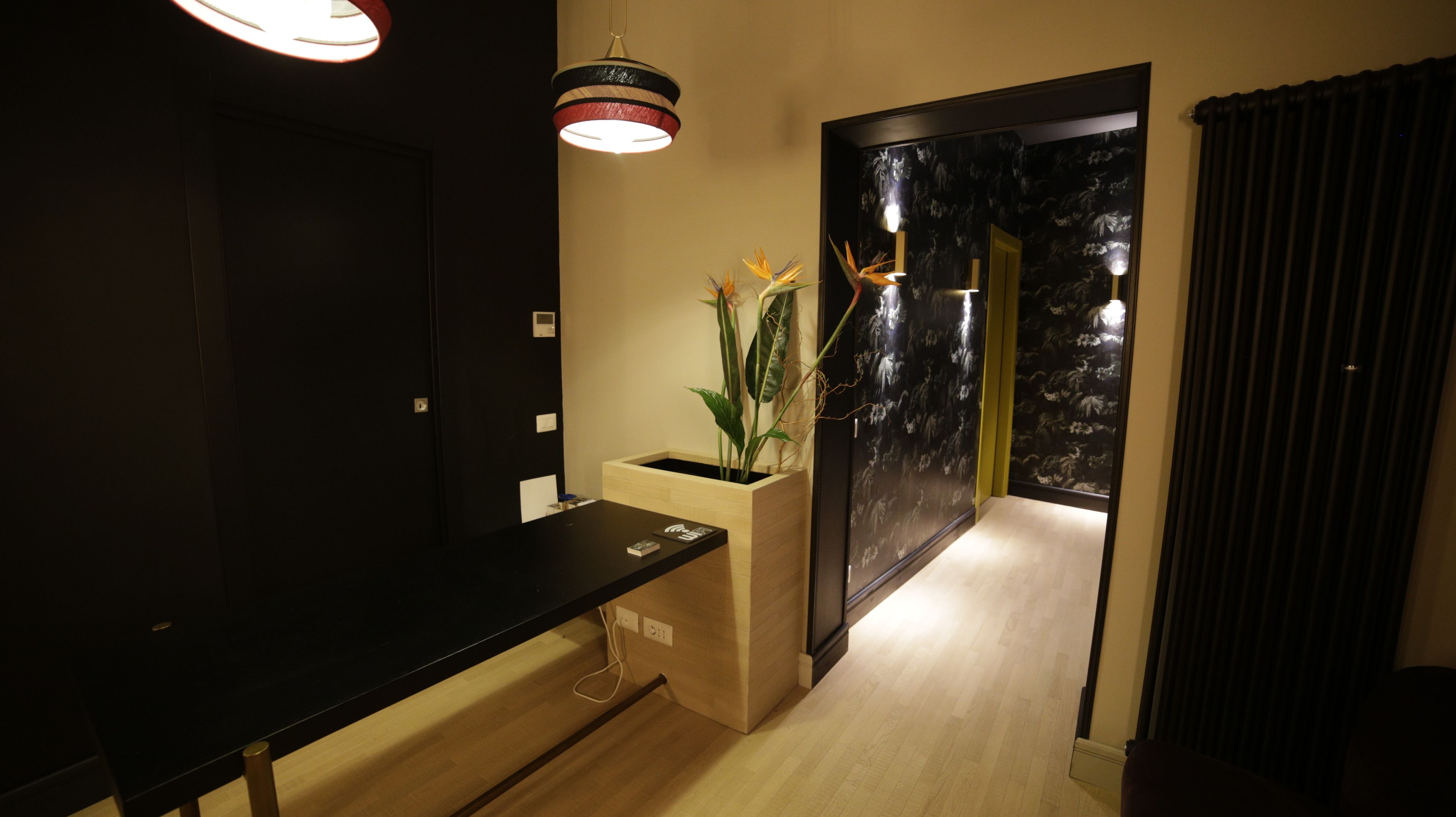 Eine moderne Hotelhalle mit einer Rezeption, einer Pflanze und einer Wand mit floralem Muster in dunklen Farben.