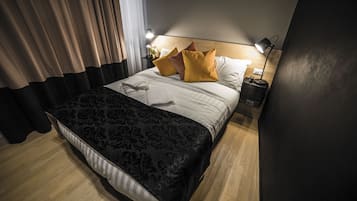 Un lit bien fait, recouvert d’une couvre-lit à motifs noir et blanc, avec un oreiller blanc et deux oreillers jaunes. Deux lampes de chevet sont placées de chaque côté du lit.