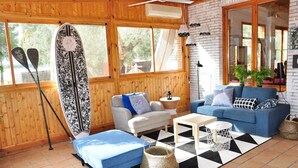 A cozy room with a blue sofa, a white armchair, and a coffee table. There is a surfboard leaning against the wall and two paddles on the floor. - Camping La Estanca (Alcaniz)