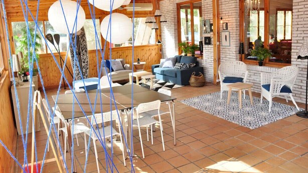 A cozy wooden cabin with a dining area, a sofa, and a large window. - Camping La Estanca (Alcaniz)