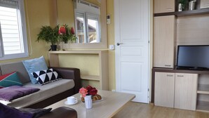 A compact living space with a sofa, a small table with a cup and flowers, a television, and a door. - Camping La Estanca (Alcaniz)