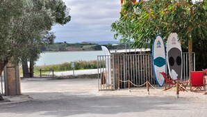 A coastal area with a view of the sea, a fenced area with a gate, and two surfboards leaning against a metal fence. - Camping La Estanca (Alcaniz)