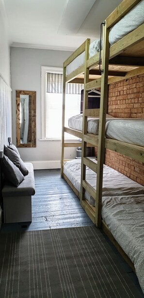 A room with bunk beds, a grey sofa, a mirror, and a window with blinds. - Bunkhouse Bournemouth - Hostel (Bournemouth)