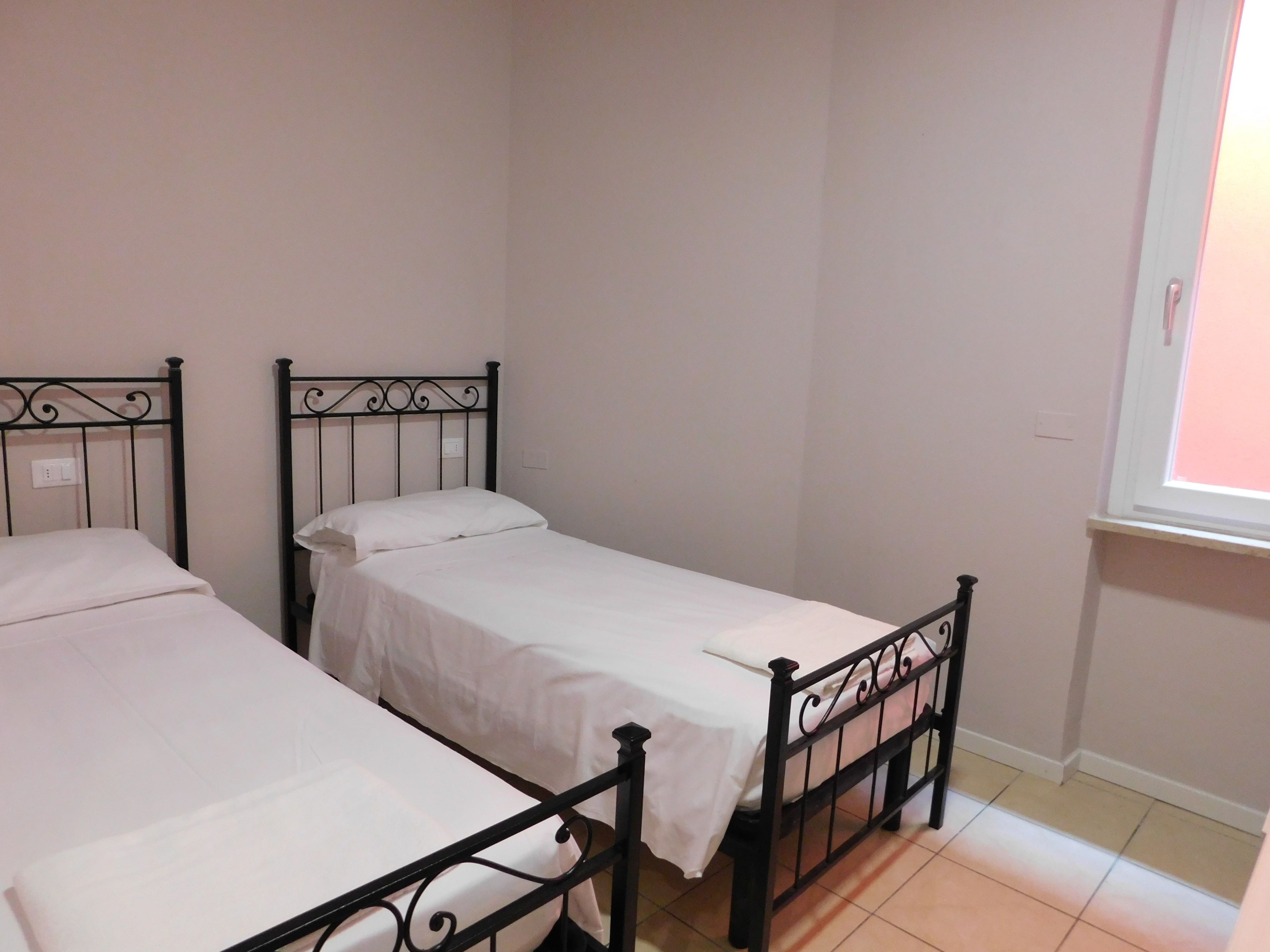 Ein Zimmer mit drei Einzelbetten, jeweils mit schwarzem Metallgestell und weißer Bettwäsche.