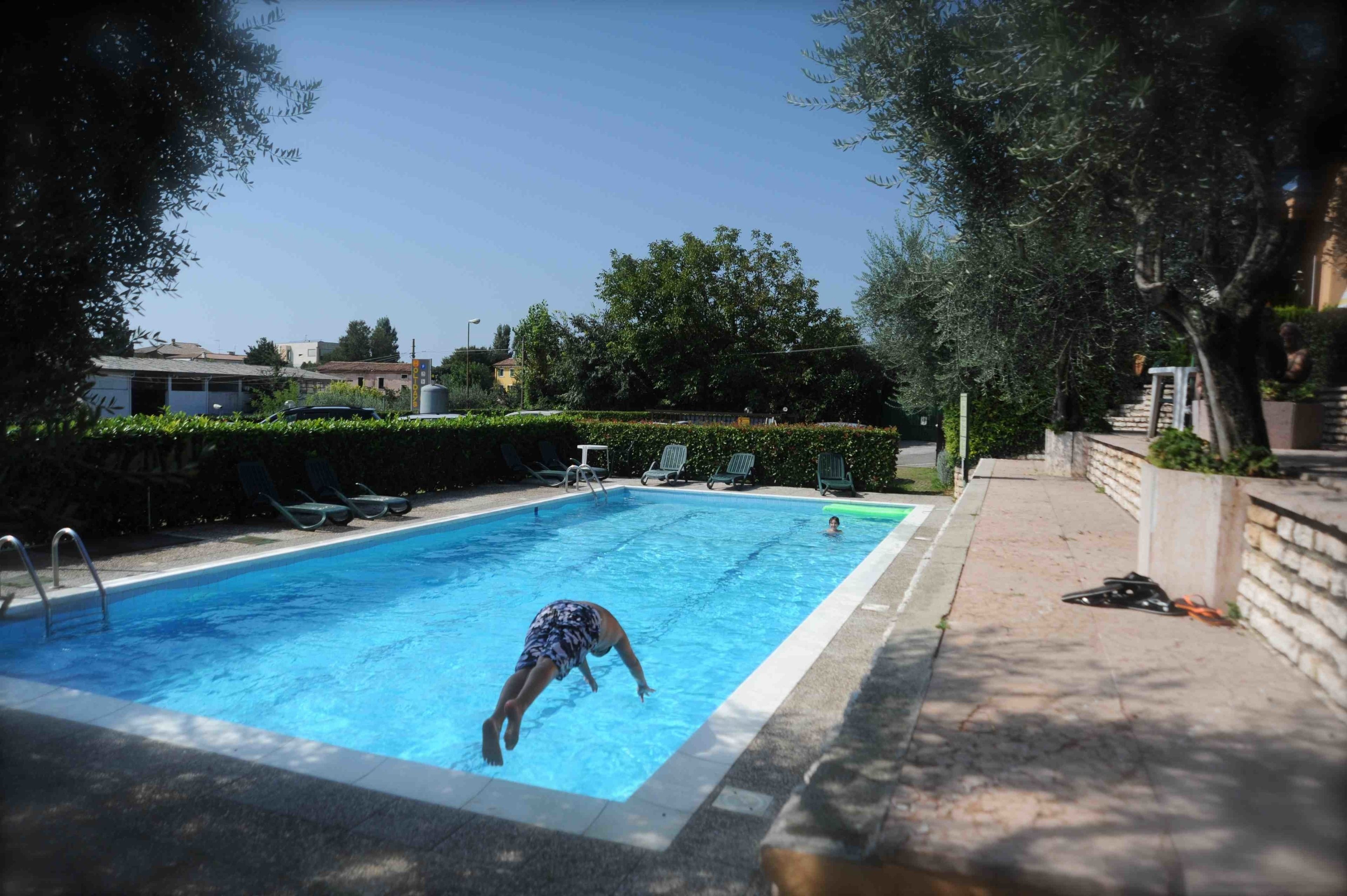 A swimming pool with a child swimming, surrounded by greenery and a paved walkway.