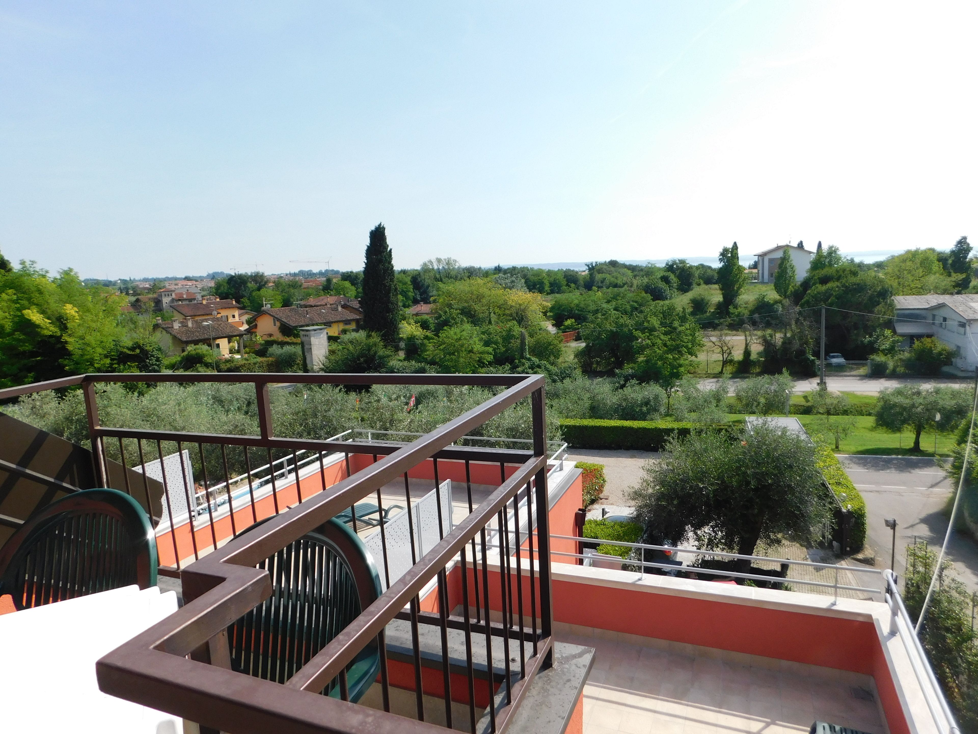 A balcony with a metal railing overlooking a residential area with houses and greenery.