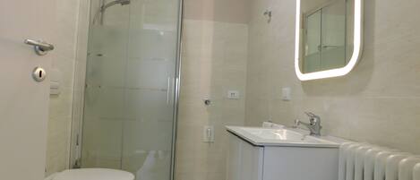 A modern bathroom with a glass-enclosed shower, a toilet, and a sink with a mirror above it.