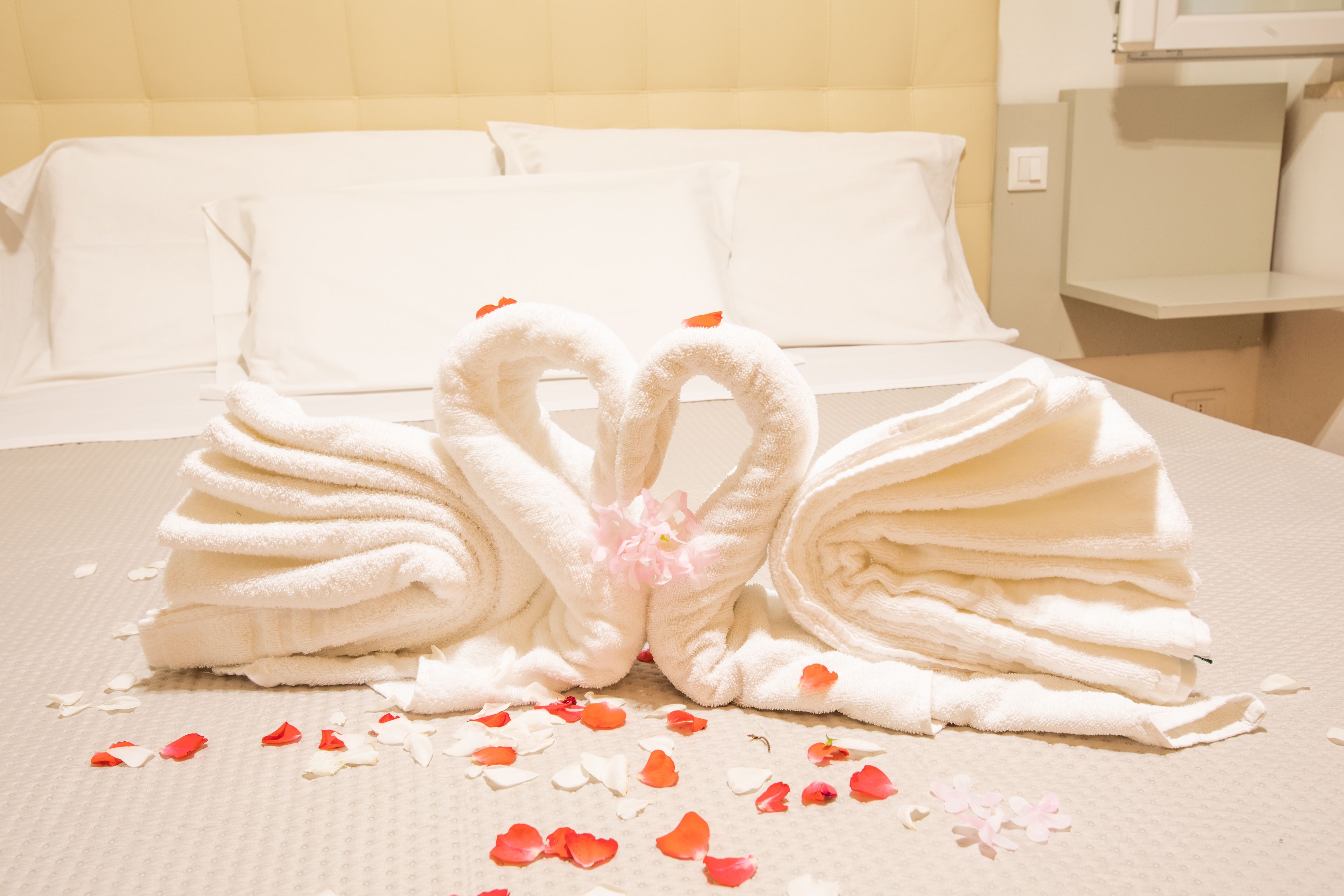 A neatly made bed with white linens and a decorative towel arrangement in the shape of swans on a textured surface.