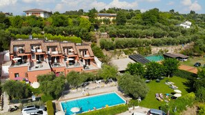 A multi-story hotel with a swimming pool, outdoor seating, and a view of the surrounding greenery. - Holidays Residence (Lazise)