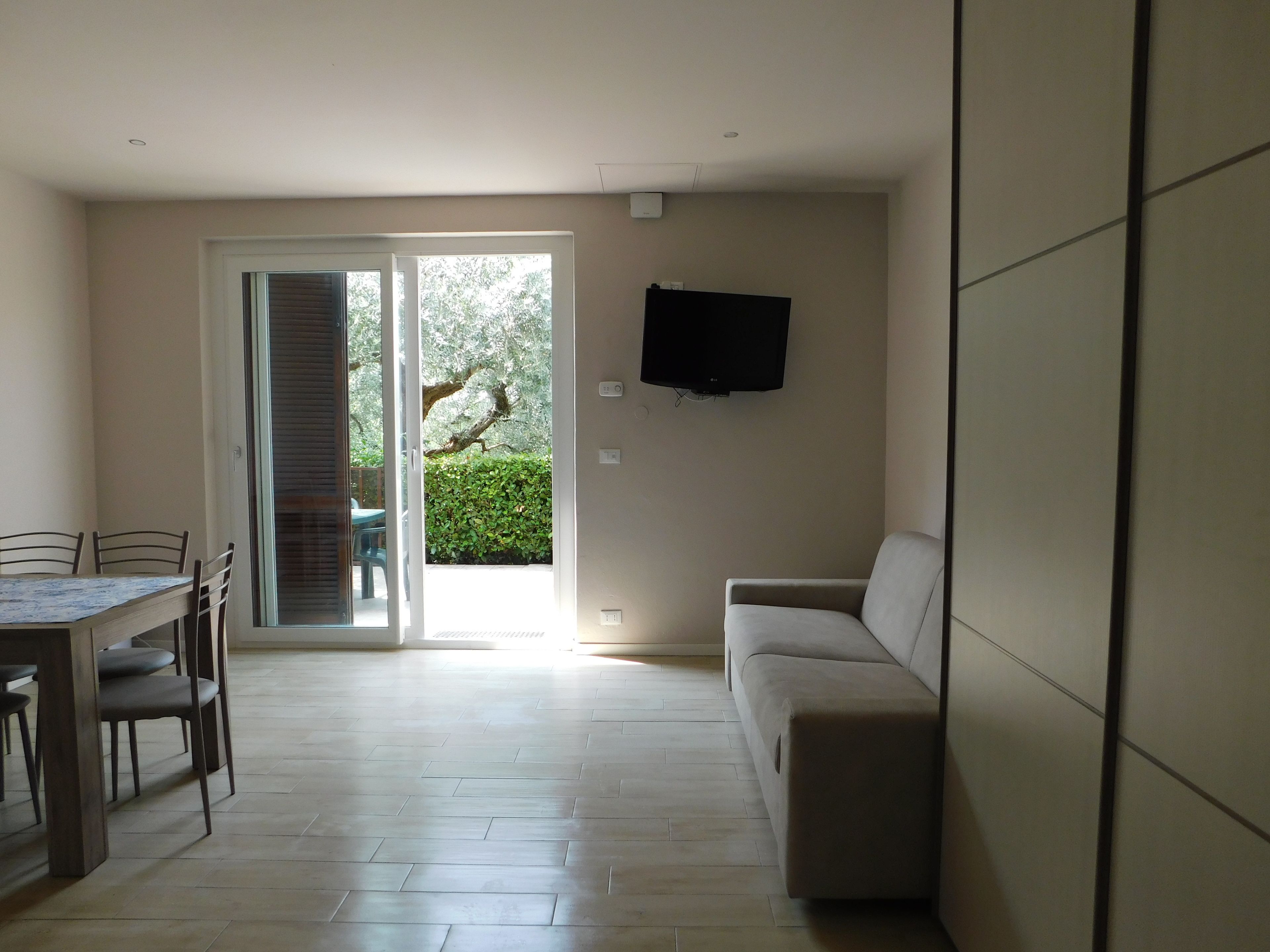Ein Wohnzimmer mit einer Couch, einem an der Wand befestigten Fernseher und einem Essbereich mit Tisch und Stühlen.
