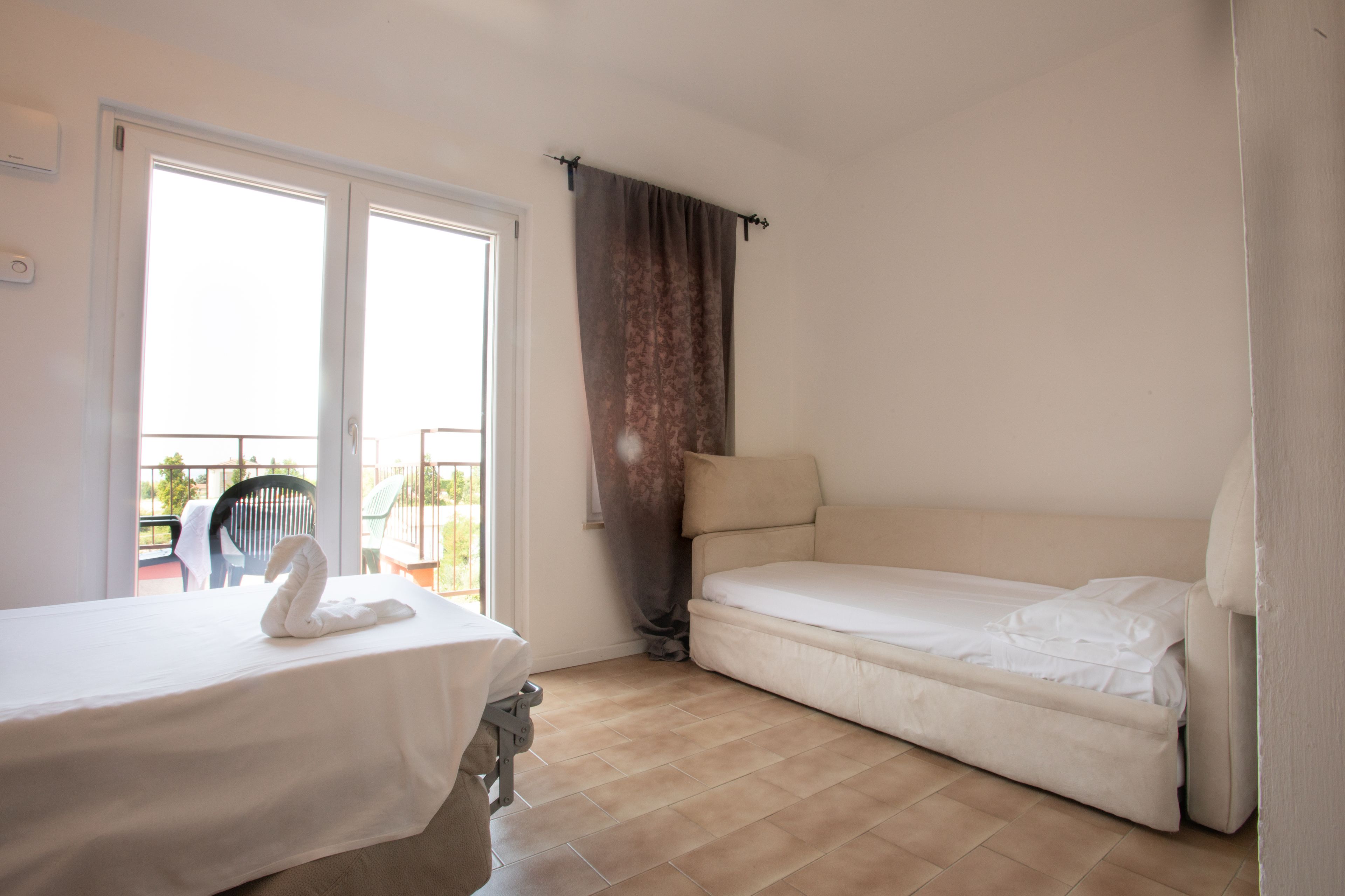 A room with a bed, a table with a swan-shaped towel, a chair, and a view of the outside.