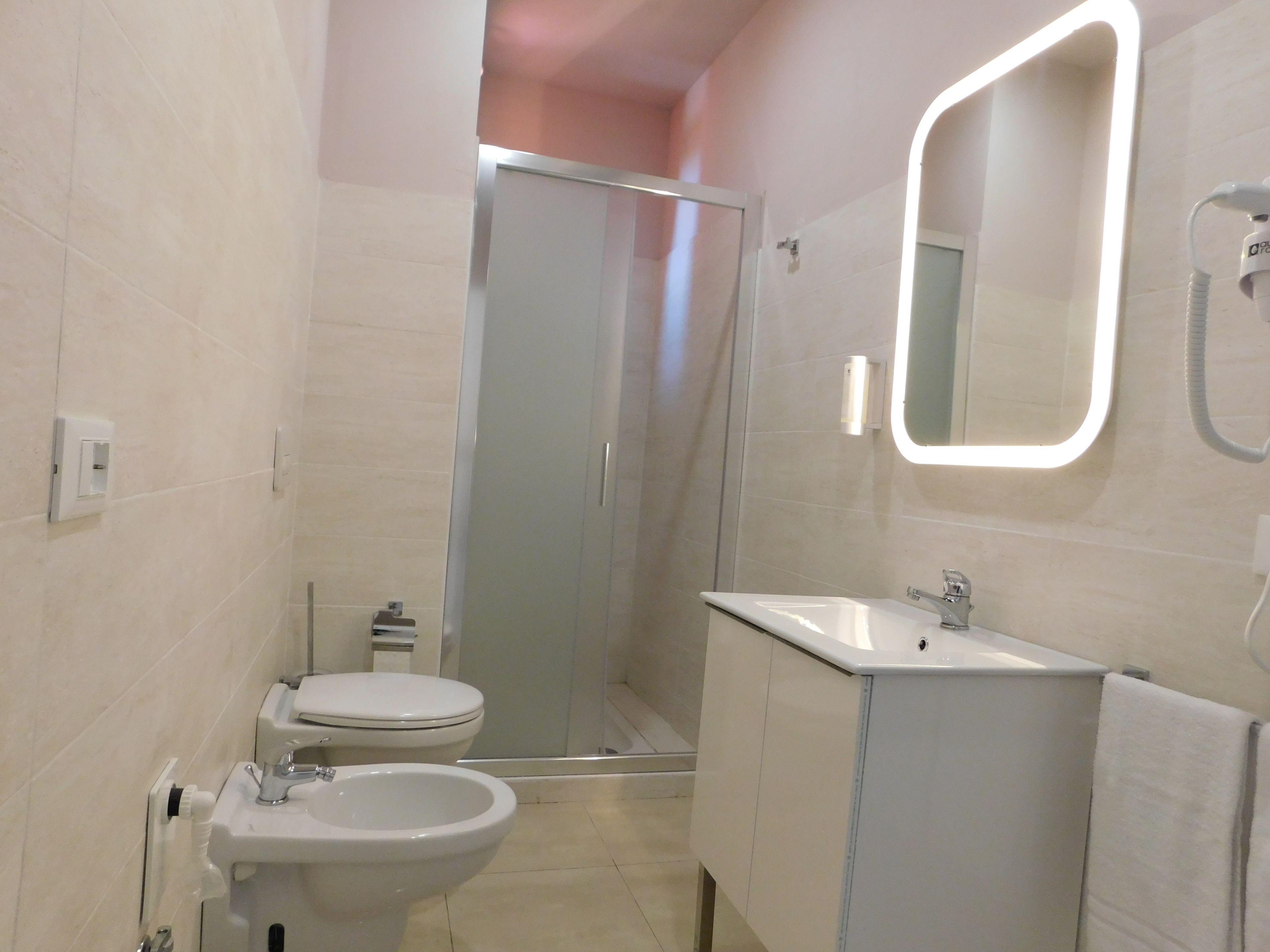 A bathroom with a toilet, bidet, sink, and a glass shower enclosure.