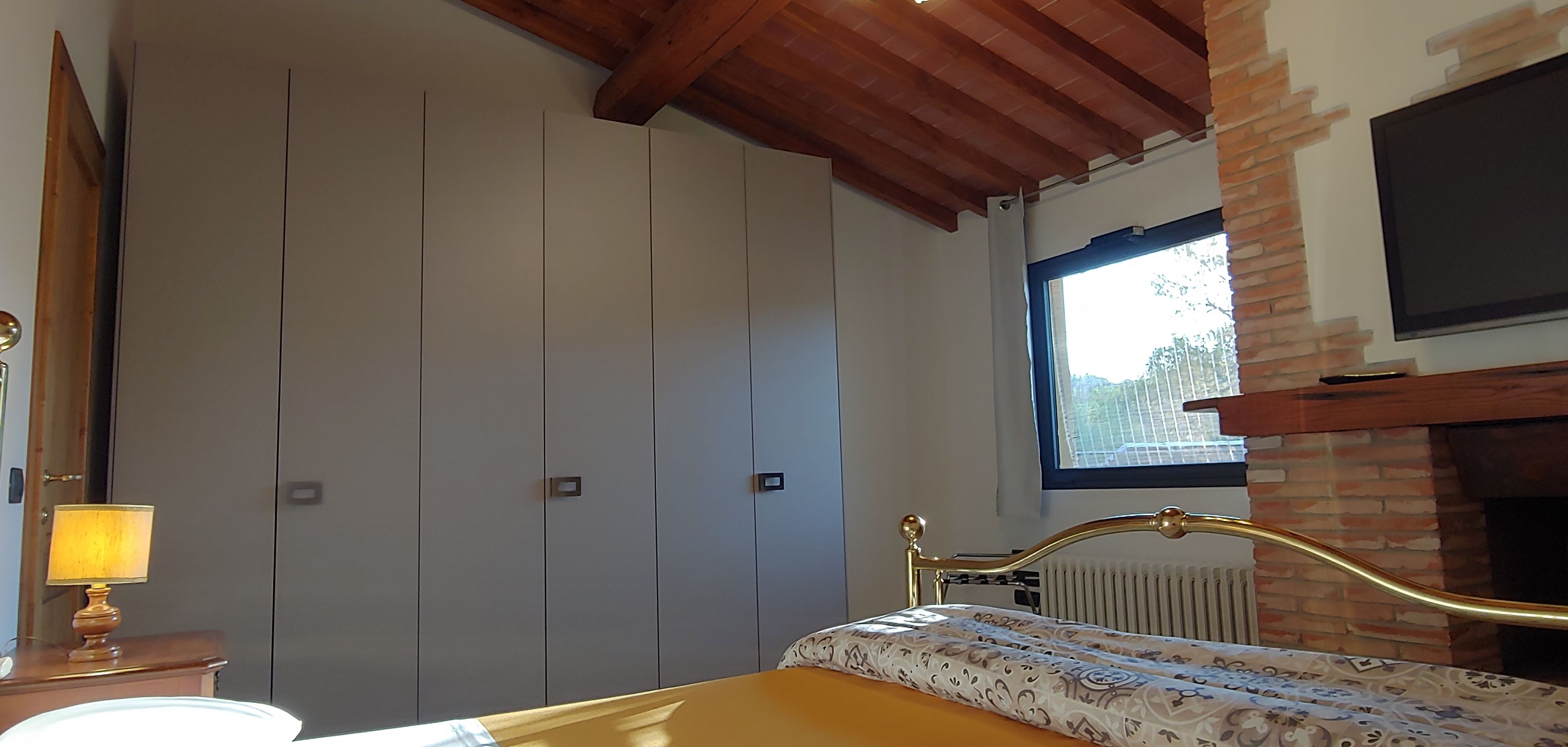 A bedroom with a bed, a lamp, a TV, and a window with a view of the outside.