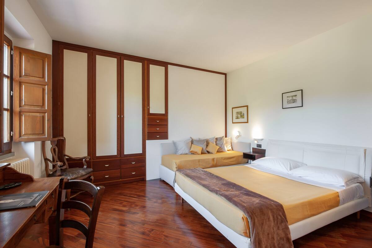 A bedroom with a double bed, wooden wardrobe, a desk with a chair, and a radiator.