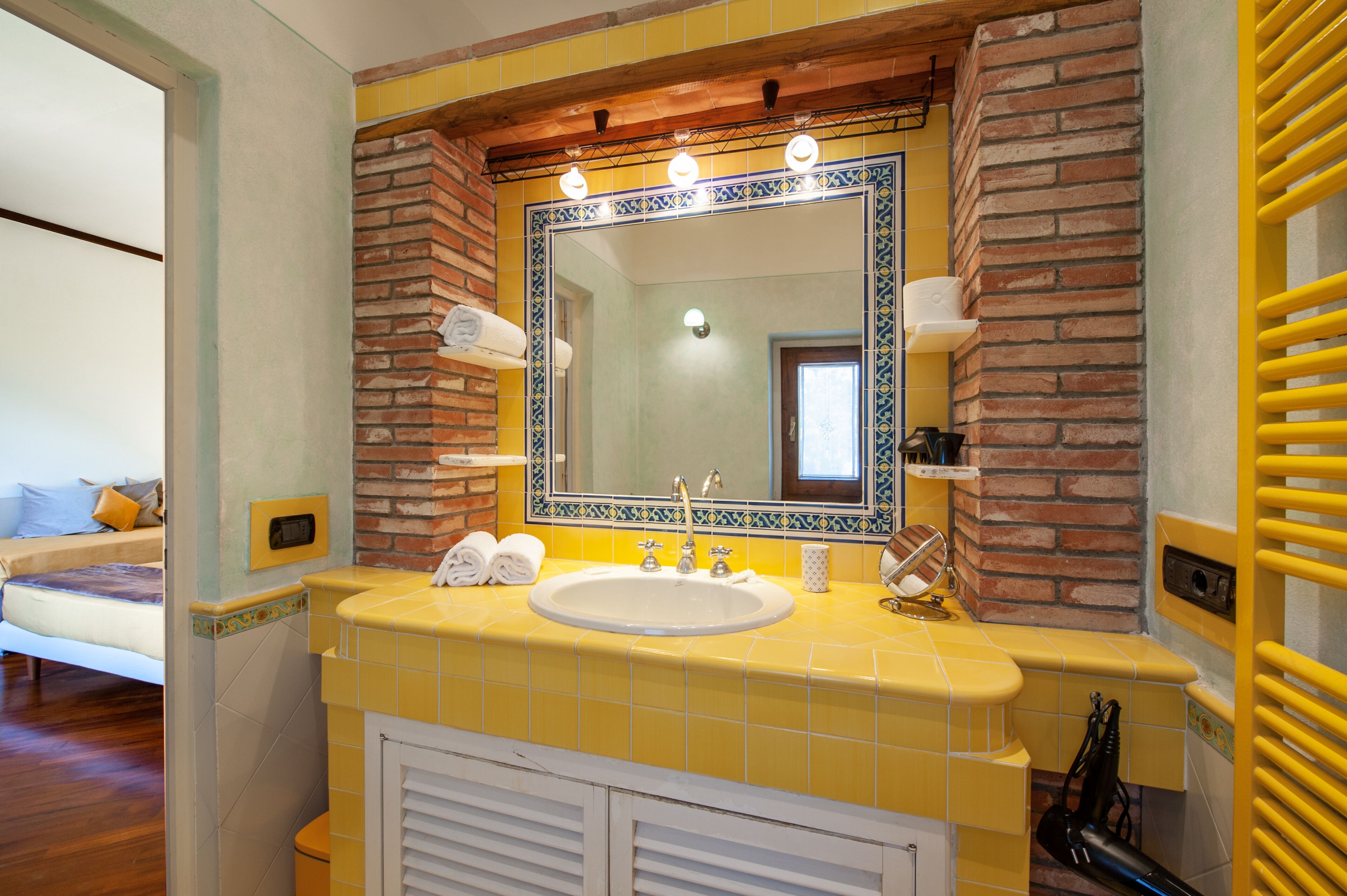 Casa de banho com lavatório amarelo, espelho grande e parede de tijolos.