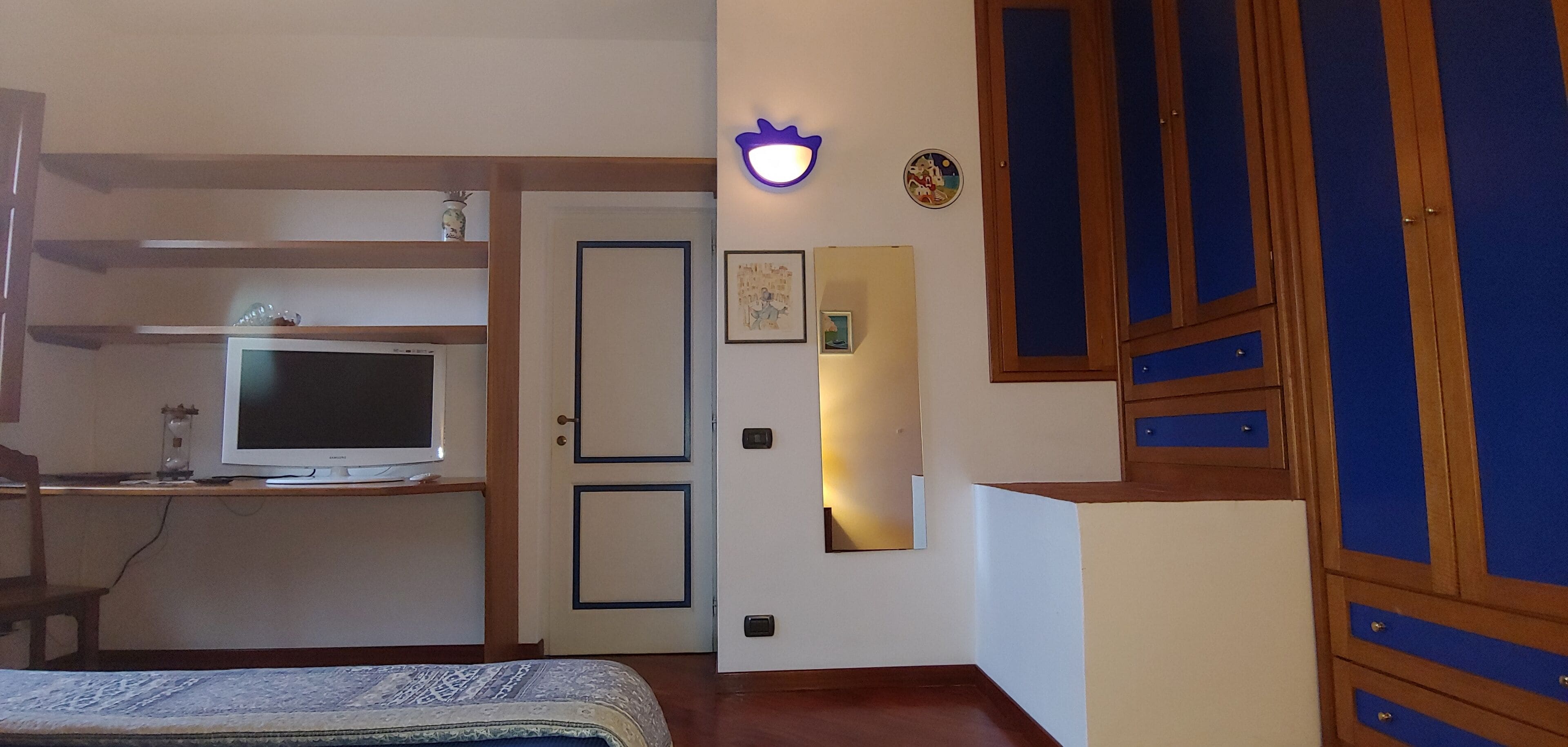 Un dormitorio con cama, televisor, armario y una puerta con espejo.