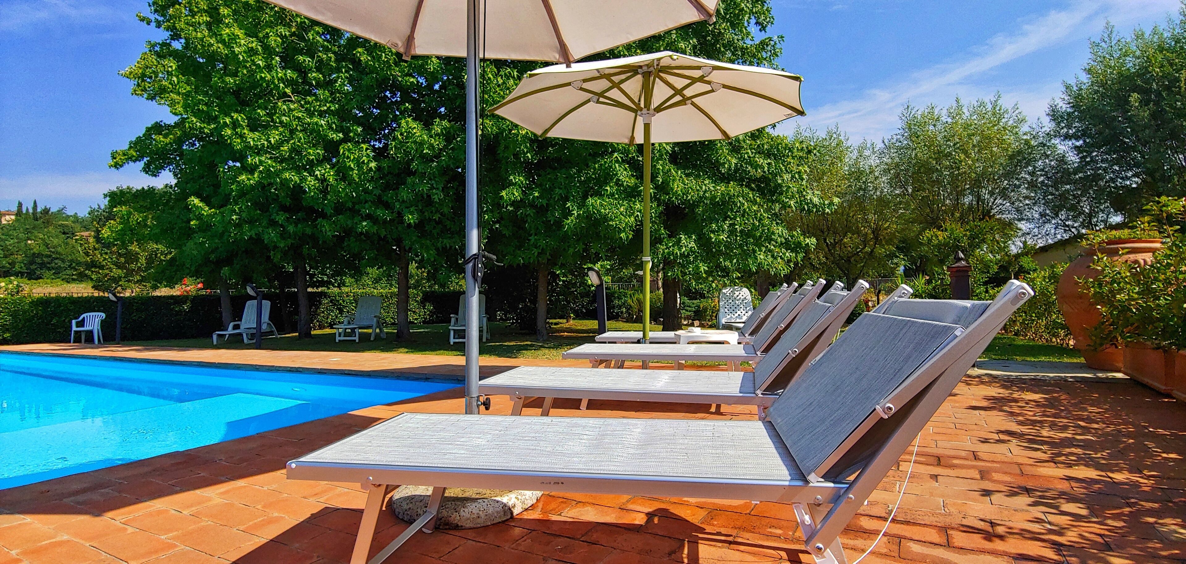Zona de piscina con sillones de descanso y una sombrilla.
