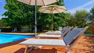 Zona de piscina con sillones de descanso y una sombrilla.