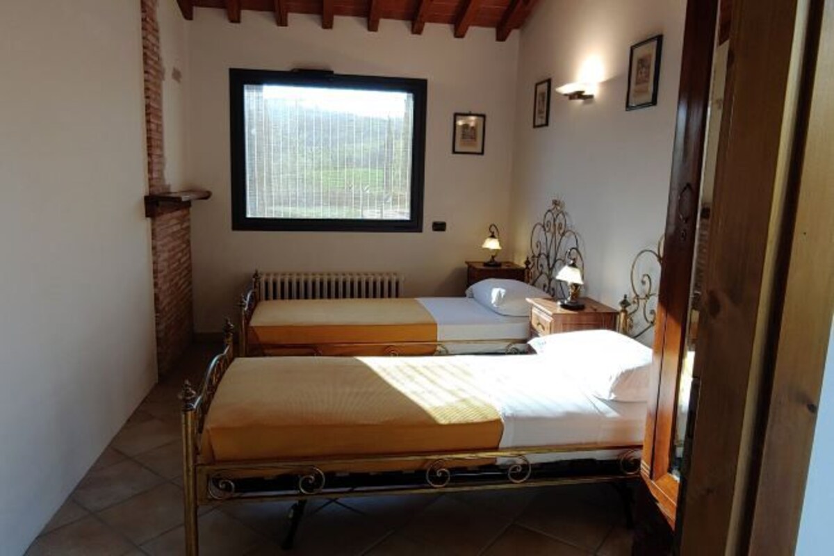 A room with two single beds, a window, a radiator, a bedside table with a lamp, and a wall-mounted picture.