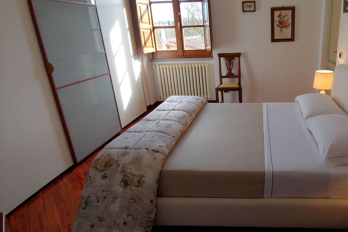 A bedroom with a bed, a chair, a radiator, a window, and a lamp.