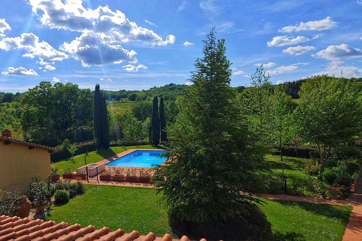 A pool surrounded by a lush garden, a clear blue sky, and a traditional building with a tiled roof.
